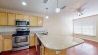 Located at 909 Apollo Beach Blvd in Apollo Beach, Florida, this single-floor residence offers a well-designed layout with a cohesive blend of practical finishes and comfortable living spaces. The open-concept living and kitchen area is anchored by rich, warm hardwood flooring that extends throughout the main living space, creating an inviting atmosphere. A ceiling fan overhead provides comfort, while recessed lighting and pendant lights above the kitchen island add both function and style. The kitchen is well-appointed with light maple cabinetry, granite countertops, a curved breakfast bar island, and a full suite of stainless steel appliances including a refrigerator, range, microwave, and dishwasher. A stacked washer and dryer unit is conveniently integrated adjacent to the kitchen. The bedrooms are carpeted for comfort and feature neutral tones, with windows that allow natural light to filter in. One bedroom includes a closet with bi-fold doors and built-in shelving. The bathroom is finished with tile flooring, a granite-topped vanity with maple cabinetry, and a tiled tub-shower combination. The overall ambiance is clean, functional, and well-maintained, making this a practical and comfortable home in the Apollo Beach community.