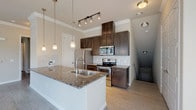 This single-story residence offers a thoughtfully designed open-concept layout that maximizes both functionality and comfort. The kitchen serves as the centerpiece of the home, showcasing rich dark-wood cabinetry, granite countertops, and a full suite of stainless steel appliances including a refrigerator, electric range, and built-in microwave. A large kitchen island with a double sink and elegant pendant lighting overhead adds both workspace and a natural gathering point. A classic white subway tile backsplash completes the polished look. Light wood-style flooring flows seamlessly throughout the living areas, enhancing the bright, airy atmosphere created by abundant natural light streaming through multiple windows adorned with white blinds. Crown molding adds a refined architectural detail to the main living and bedroom areas. The bedroom is generously proportioned, featuring a large window that invites natural light and views of the surrounding neighborhood. The full bathroom is equipped with a soaking tub and overhead shower combination, framed by large-format subway tiles, alongside a granite-topped dark vanity with a single sink and a wide mirror. A private exterior door off the main living area provides convenient outdoor access, rounding out this well-designed and move-in-ready home.