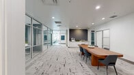 Located at 101 Lake Ave in downtown Orlando, this thoughtfully designed office suite delivers a polished, contemporary work environment across a single floor. Floor-to-ceiling glass partitions with sleek black aluminum framing define the private offices and conference spaces, maintaining an open, light-filled atmosphere throughout. A distinctive textured carpet in neutral tones anchors the space cohesively from room to room.

The formal conference room is a standout feature, accommodating a large rectangular table beneath dramatic circular pendant lighting. Floor-to-ceiling windows line the perimeter, offering abundant natural light and views of the surrounding urban greenery. Adjacent glass walls connect to the wider suite while displaying vibrant abstract artwork.

A central lounge and collaboration area features a warm walnut conference table paired with modern upholstered chairs and a built-in kitchenette with white cabinetry and a dark accent wall. This space serves as a versatile hub for informal meetings and daily operations.

The five private offices are bright and well-appointed, several featuring large exterior windows with views toward Lake Avenue. One office highlights a bold teal accent wall, adding a touch of personality. Connecting hallways are wide and open, enhancing circulation and the overall sense of flow throughout this professional, move-in-ready suite.
