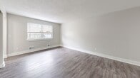 Located at 4 Valley Brook Cir in Rochester, NY, this multi-floor home offers a well-organized layout spread across three levels, providing comfortable living spaces throughout. The main level welcomes residents through an entrance that opens into a spacious living room, where wide-plank, hardwood-style flooring and neutral gray walls create a bright, airy atmosphere. Large windows allow natural light to fill the room, offering views of the surrounding greenery. The kitchen is efficiently designed with white shaker cabinetry, subway tile backsplash, light countertops, stainless steel appliances including a range and built-in microwave, and matching hardwood-style flooring. Both bedrooms feature plush carpeting, soft neutral tones, and generous closet space — the primary bedroom notably includes a double sliding-door closet spanning an entire wall. Each bedroom is served by windows that bring in natural light. The two bathrooms are finished with wood-look flooring, white vanities, and full tub-shower combinations with brushed nickel hardware. A utility room on the lower level provides additional functional space, while a staircase connects all three floors. The home's clean, contemporary palette and thoughtful floor plan make it a comfortable and practical residence.
