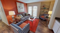 Located at 4001 W Northgate Dr in Irving, Texas, this single-floor residence offers a thoughtfully designed layout with a warm and vibrant character throughout. The living room makes an immediate impression with its rich terracotta accent wall, wood-style flooring, and French doors fitted with plantation shutters that invite natural light and provide access to an outdoor area. Built-in shelving in the corner adds both storage and display functionality to the space. The dining area is defined by a sophisticated pendant light overhead, a cool-toned accent wall, and a pass-through window connecting directly to the kitchen, creating a seamless flow between rooms. The kitchen features white cabinetry, dark countertops, wood-style flooring, and black appliances including a range, microwave, and dishwasher, offering a practical and clean workspace. Both bedrooms are carpeted and well-sized, each featuring windows with blinds that allow natural light. The primary bedroom includes a ceiling fan and direct access to a spacious walk-in closet, while the second bedroom also offers generous closet space. The bathroom is equipped with a wide vanity featuring ample cabinet storage, a large mirror with a lighted fixture above, and a combination shower and soaking tub.