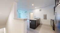 This single-floor unit showcases a clean, contemporary design throughout, with crisp white walls, light wood-style flooring, and recessed lighting that contribute to a bright and airy atmosphere. The open-concept kitchen serves as a central highlight, anchored by a large island with a granite countertop, undermount sink, and a sleek faucet. Dark espresso cabinetry provides striking contrast against the light surroundings, while a full suite of stainless steel appliances — including a side-by-side refrigerator with ice maker, electric range, over-the-range microwave, and dishwasher — ensures full functionality. A tile backsplash adds a refined finishing touch. The living area offers generous open space, complete with a ceiling fan and a window that brings in natural light. The bedroom is similarly well-lit, featuring a ceiling fan, a window with exterior views, and direct access to additional spaces. The bathroom includes a dark-cabineted vanity with a granite countertop, a framed mirror, and a full tub-shower combination. A dedicated laundry room houses a stacked GE washer and dryer unit alongside overhead shelving for storage.