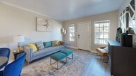 Located at 227 Eisenhower Dr in Biloxi, Mississippi, this single-floor unit offers a thoughtfully designed layout with 1 bedroom, 2 bathrooms, and four closets for ample storage. The open living and dining area is finished with light hardwood-style flooring throughout and features crown molding, a ceiling fan, and multiple windows that bring in generous natural light. The living space comfortably accommodates both a seating and dining area, with the kitchen accessible just beyond. The kitchen is equipped with black appliances, including a refrigerator and electric range, set against white upper cabinetry and gray lower cabinetry with a tile backsplash. A pass-through window connects the kitchen to an adjacent hallway, enhancing the open feel. The bedroom is a comfortable, well-proportioned retreat with a ceiling fan, a window with blinds, and hardwood-style flooring. The bathrooms feature gray vanity cabinetry with light countertops, offering a clean, contemporary aesthetic. A utility room and dedicated closets throughout the unit provide practical storage solutions. The entry features a modern smart lock and flanking windows that invite outdoor light into the home, creating a bright and welcoming atmosphere from the moment you step inside.