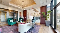 Located at 2180 Pickens Street in Columbia, South Carolina, this thoughtfully designed amenity space offers a generous single-floor layout that seamlessly blends elegance with functionality. The welcoming lobby lounge serves as the heart of the space, showcasing wide-plank hardwood flooring, a coffered ceiling with a textured gold inlay, and a striking Sputnik chandelier that anchors the room. Deep burgundy paneled walls contrast beautifully with crisp white surfaces, while emerald green velvet wingback chairs, a curved cream sofa, and richly hued area rugs contribute to the eclectic yet refined aesthetic. Floor-to-ceiling windows flood the space with natural light and frame sweeping views of the outdoor pool and courtyard. A reception counter adorned with globe pendant lighting adds a boutique hotel-like quality to the main area. The two dining rooms offer intimate settings for small gatherings, each distinguished by textured metallic wallcovering, a walnut dining table with nailhead-trimmed upholstered chairs, and statement chandeliers—one beaded globe and one Sputnik style. Bold botanical and abstract murals provide artistic focal points, and a wall-mounted display screen with built-in cabinetry enhances versatility. Together, these spaces deliver a polished and inviting environment suited for socializing, meetings, and everyday community life.