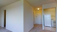 This single-floor residence offers a straightforward and functional layout designed for comfortable everyday living. The entryway sets the tone for the space, featuring a solid entry door framed by light-colored walls and a flush ceiling light fixture that provides a warm, welcoming glow. The corridor leading into the space is well-proportioned, creating a smooth transition between the entrance and the rest of the home. Neutral, light-colored walls are consistent throughout, lending a clean and airy feel to the interior. Wall switch plates and outlet covers are thoughtfully placed, reflecting a practical design sensibility. The flooring consists of wall-to-wall carpeting in a soft, muted tone, contributing to a cozy and quiet atmosphere underfoot. A glimpse into an adjoining area hints at additional living space, suggesting an open and connected floor plan. The overall ambiance is calm and understated, with an emphasis on simplicity and utility. This space presents a solid foundation that is move-in ready and easily personalized to suit a variety of tastes and lifestyles.