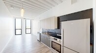 Located at 1135 N Sheridan in Chicago's Edgewater neighborhood, this contemporary single-floor residence showcases a thoughtfully designed interior that blends modern finishes with architectural character. Throughout the space, striking exposed beam ceilings painted crisp white lend a sense of volume and industrial-chic elegance, complemented by light-toned hardwood-style flooring that runs seamlessly from room to room.

The kitchen is a standout feature, equipped with a full suite of stainless steel appliances including a range, dishwasher, and full-size refrigerator. Two-toned cabinetry — pairing light upper cabinets with darker lower units — frames sleek dark granite countertops and a coordinating backsplash, creating a polished, cohesive aesthetic. A large-format window at the end of the kitchen draws in generous natural light.

The bedroom is a bright, airy retreat anchored by dramatic floor-to-ceiling windows with bold black frames, offering expansive views of the Chicago skyline and surrounding neighborhood. The open layout provides flexible furnishing options, while the adjacent space features a walk-in closet area.

The bathroom is finished with a warm wood-toned vanity topped with a richly veined dark marble countertop, an undermount sink, and a sleek vertical mirror. A glass-enclosed shower completes this well-appointed room. The overall ambiance is clean, modern, and filled with natural light.