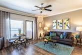 Located at 21626 Stonewall Pkwy in San Antonio, TX, this 1-bedroom, 1-bathroom residence offers a well-designed, single-floor layout that blends modern finishes with comfortable living. The open-concept living and dining area features rich hardwood-style flooring, crown molding, and a ceiling fan, creating a warm and inviting atmosphere. Large glass doors flood the space with natural light and lead to a private balcony, extending the living area outdoors.

The kitchen is equipped with stainless steel appliances, including a side-by-side refrigerator, electric range, and microwave. Dark espresso cabinetry pairs with granite countertops and a subway tile backsplash, while a breakfast bar with a double-basin sink connects the kitchen to the living area. Pendant lighting and a track light fixture provide both task and ambient illumination.

The bedroom offers plush carpeting, a ceiling fan, and natural light from windows with blinds. It connects directly to the spacious bathroom, which features a double-sink vanity with granite countertops, tile flooring, a walk-in shower, and a generously sized walk-in closet. Throughout the residence, bold navy interior doors add a distinctive design touch that ties the space together cohesively.