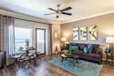 Located at 21626 Stonewall Pkwy in San Antonio, TX, this 1-bedroom, 1-bathroom residence offers a well-designed, single-floor layout that blends modern finishes with comfortable living. The open-concept living and dining area features rich hardwood-style flooring, crown molding, and a ceiling fan, creating a warm and inviting atmosphere. Large glass doors flood the space with natural light and lead to a private balcony, extending the living area outdoors.

The kitchen is equipped with stainless steel appliances, including a side-by-side refrigerator, electric range, and microwave. Dark espresso cabinetry pairs with granite countertops and a subway tile backsplash, while a breakfast bar with a double-basin sink connects the kitchen to the living area. Pendant lighting and a track light fixture provide both task and ambient illumination.

The bedroom offers plush carpeting, a ceiling fan, and natural light from windows with blinds. It connects directly to the spacious bathroom, which features a double-sink vanity with granite countertops, tile flooring, a walk-in shower, and a generously sized walk-in closet. Throughout the residence, bold navy interior doors add a distinctive design touch that ties the space together cohesively.