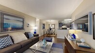 This single-story, 2-bedroom, 2-bathroom residence offers a smart, functional layout designed to maximize comfort and livability. The open-concept living area features rich hardwood-style flooring, neutral warm-toned walls, and large sliding glass doors dressed with vertical blinds that invite natural light while providing outdoor views. The living room flows seamlessly into the dining area and kitchen, creating a cohesive entertaining space. The kitchen is equipped with dark espresso cabinetry, a mosaic tile backsplash, black appliances including a refrigerator and range, and a peninsula with a granite-style countertop that doubles as a breakfast bar. The adjacent dining nook accommodates a round glass-top table beneath a pendant light fixture. Both bedrooms are carpeted and well-proportioned, with the primary bedroom featuring a ceiling fan and a connecting bathroom. The second bedroom is equally comfortable with ample natural light. Each bathroom includes a full tub-and-shower combination with crisp white surrounds and wood-style flooring. Two closets provide dedicated storage throughout. The overall ambiance is clean and contemporary, with consistent design choices tying each room together in a welcoming, move-in-ready presentation.