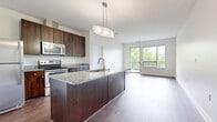Located at 300 Riverboat Row in Newport, Kentucky, this well-appointed 2-bedroom, 2-bathroom residence offers a thoughtfully designed single-level layout with modern finishes throughout. The open-concept kitchen and living area serves as the heart of the home, anchored by a large center island topped with granite countertops and fitted with an integrated sink and pendant lighting. Rich dark-wood cabinetry, a full suite of stainless steel appliances—including a refrigerator, electric range, and over-the-range microwave—and a subway tile backsplash complete the kitchen. The living area extends naturally from the kitchen, bathed in natural light from expansive windows and a sliding glass door that opens to an outdoor balcony with leafy views. Hardwood-style flooring runs throughout the main living spaces, while plush carpeting adds comfort to both bedrooms. The generously sized primary bedroom features a ceiling fan and a window with outdoor views. The bathrooms are finished with large-format tile flooring, dark granite vanity tops, and rich wood cabinetry. A dedicated laundry area with a stacked washer/dryer and water heater provides added convenience. Two closets offer ample storage throughout the residence.