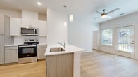 Located at 5900 S Congress Ave in Austin, TX, this well-designed two-bedroom, two-bathroom unit offers a thoughtful single-floor layout with a clean, contemporary aesthetic. Light wood-tone flooring runs throughout, complementing the crisp white walls and creating a bright, cohesive atmosphere.

The open-concept kitchen and living area serves as the heart of the unit. The kitchen is outfitted with stainless steel appliances—including a refrigerator with ice maker, electric range, over-the-range microwave, and dishwasher—alongside two-tone cabinetry in white and warm wood finishes, a white quartz countertop peninsula with an undermount sink, and a classic subway tile backsplash. Pendant lighting over the peninsula and a ceiling fan in the living area add functional style. The living space features direct outdoor access through a glass door flanked by windows, filling the room with natural light.

Both bedrooms are well-proportioned, each with a ceiling fan, natural light from windows with blinds, and generous closet space—including a walk-in closet with wire shelving. The primary bedroom offers a notably spacious footprint. The two bathrooms feature matching wood-tone vanities with white countertops, tub-shower combinations with tile surrounds, and overhead cabinetry for storage. The unit also includes a dedicated laundry area and utility room for added convenience.
