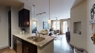 This thoughtfully designed single-floor residence offers a seamless open-concept layout that connects the kitchen, dining, and living areas into one cohesive, functional living space. The kitchen is a standout feature, showcasing granite countertops, rich dark cabinetry, a stainless steel double sink, pendant lighting, and a full suite of stainless steel appliances including a refrigerator with ice maker, range, and built-in microwave. A breakfast bar provides additional seating and further integrates the kitchen with the dining area, which is accented by warm wood flooring and a decorative full-length mirror.

The living room is bright and inviting, benefiting from large floor-to-ceiling windows and a glass door that flood the space with natural light and offer views to the outside. A ceiling fan and track lighting add functional ambiance throughout. The bedroom is a comfortable retreat, carpeted for warmth, with a ceiling fan and a window that lets in natural light. The full bathroom features a tiled tub-shower combination with a curved curtain rod and dark wood vanity with granite countertop. Completing the unit is a dedicated laundry area equipped with a full-size washer and dryer and built-in shelving for storage.
