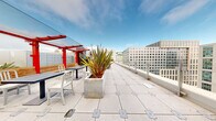 Located at 33 8th Street in San Francisco's SoMa district, this rooftop deck offers an expansive open-air environment with sweeping panoramic views of the city skyline, surrounding neighborhoods, and distant hills. The deck's large-format granite tile flooring extends across the entire level, providing a clean, modern aesthetic throughout.

Distinctive red pergola structures serve as architectural focal points, framing dedicated seating areas furnished with contemporary outdoor lounge chairs, sofas, and café-style tables and chairs. These covered zones offer partial shade while maintaining an open connection to the sky. Multiple raised concrete and stone planters are distributed across the deck, filled with ornamental grasses, agave, and other drought-tolerant plants that add greenery and visual texture to the space.

Glass and metal perimeter railings ensure unobstructed sightlines across San Francisco's urban landscape, while coin-operated binoculars are available at designated viewing points to explore the cityscape in detail. Raised garden beds with low-profile seating ledges provide additional gathering spots. The deck is sectioned into distinct zones, including open promenades and intimate lounge areas, creating a versatile outdoor environment suited to both active use and quiet relaxation.