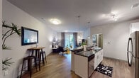 This well-appointed single-story residence offers a thoughtfully designed open-concept layout that seamlessly connects the kitchen, dining, and living areas. The kitchen is a standout feature, equipped with white shaker-style cabinetry, dark granite countertops, a subway tile backsplash, stainless steel appliances including a refrigerator, range, and microwave, and a central island with seating for two. Elegant pendant lighting illuminates the island, complementing the warm hardwood-style flooring that runs throughout the main living areas. The living room is bright and welcoming, featuring a sliding glass door that opens to a private outdoor patio and allows abundant natural light to fill the space. A casual dining area sits adjacent to the kitchen, offering additional seating options. The bedrooms are carpeted for comfort and feature large windows with sheer curtains that invite natural light, along with stylish panel doors and ceiling fans. The bathroom includes a full soaking tub and shower combination, a granite-topped vanity with white cabinetry, and tile flooring. Neutral tones and clean lines throughout the residence create a cohesive, modern aesthetic that is both functional and inviting.