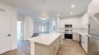 Located at 25 Silver Moon Circle in St. Augustine, FL, this well-appointed single-story home offers a bright, modern design across three bedrooms and two bathrooms. The open-concept living area seamlessly connects the kitchen, dining, and living spaces, all finished with light wood-look flooring that flows throughout. The kitchen is a standout feature, boasting crisp white cabinetry extending to the ceiling, a large center island with quartz countertops, subway tile backsplash, and a full suite of stainless steel appliances. Pendant lighting and recessed fixtures illuminate the space beautifully. The living room is airy and welcoming, with a ceiling fan and glass French doors that invite natural light and provide outdoor access. The primary bedroom offers a generous footprint with its own walk-in closet equipped with wire shelving. Additional bedrooms are well-sized, each with closet access and large windows with outdoor views. The bathrooms are finished in a clean, contemporary style, with one featuring large-format tile flooring, a glass-enclosed walk-in shower with subway tile surround, and a sleek floating vanity. The home also includes a dedicated laundry area, utility room, and ample closet storage throughout.