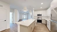 Located at 25 Silver Moon Circle in St. Augustine, FL, this well-appointed single-story home offers a bright, modern design across three bedrooms and two bathrooms. The open-concept living area seamlessly connects the kitchen, dining, and living spaces, all finished with light wood-look flooring that flows throughout. The kitchen is a standout feature, boasting crisp white cabinetry extending to the ceiling, a large center island with quartz countertops, subway tile backsplash, and a full suite of stainless steel appliances. Pendant lighting and recessed fixtures illuminate the space beautifully. The living room is airy and welcoming, with a ceiling fan and glass French doors that invite natural light and provide outdoor access. The primary bedroom offers a generous footprint with its own walk-in closet equipped with wire shelving. Additional bedrooms are well-sized, each with closet access and large windows with outdoor views. The bathrooms are finished in a clean, contemporary style, with one featuring large-format tile flooring, a glass-enclosed walk-in shower with subway tile surround, and a sleek floating vanity. The home also includes a dedicated laundry area, utility room, and ample closet storage throughout.