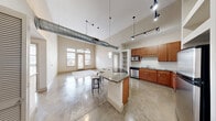 Located at 800 Lake Carolyn Pkwy in Irving, TX, this 2-bedroom, 2-bathroom loft-style residence offers a striking open-concept design across a single floor. The living and kitchen areas share a dramatic, soaring ceiling with exposed industrial ductwork and track lighting, lending a modern urban character throughout. Polished concrete floors extend across the main living space, anchoring the layout with a sleek, durable finish.

The kitchen is well-appointed with warm wood cabinetry, granite countertops, a subway tile backsplash, and stainless steel appliances. A curved granite-topped island with a built-in cooktop serves as a functional centerpiece, offering seating and additional prep space. Open built-in shelving provides convenient storage adjacent to the kitchen.

The living area benefits from large windows and direct patio access, allowing ample natural light and outdoor connectivity. Both bedrooms feature plush carpeting, generous windows with blinds, and ceiling fans. The spacious primary bedroom connects to an en-suite bathroom with granite vanity, a glass-enclosed shower, and a walk-in closet with wire shelving. Three total closets and a dedicated laundry room enhance everyday functionality throughout this well-designed urban residence.
