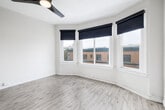 Located at 1831-1835 Harmon St in Berkeley, CA, this single-room space offers a thoughtfully designed bedroom with a clean, modern aesthetic. The standout architectural feature is a graceful curved bay window arrangement fitted with large, multi-pane windows dressed in sleek black roller shades. This bay fills the room with an abundance of natural light while offering open views of the surrounding Berkeley neighborhood and streetscape.

The room is finished with light hardwood-style flooring that complements the crisp white walls and white baseboard trim, lending the space a fresh, airy feel. A ceiling fan with an integrated light fixture provides both comfort and additional illumination. A full-length mirror is incorporated into one of the interior doors, adding a functional and stylish touch.

Storage is addressed by a built-in closet with shelving and a hanging rod, keeping the room practical and organized. A second interior door connects the room to the adjacent hallway or common area, contributing to an efficient layout. The neutral color palette throughout creates a versatile backdrop easily adaptable to a variety of furnishing styles. Overall, the space presents a comfortable and light-filled bedroom with character-rich architectural details in a well-situated Berkeley location.