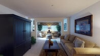 This single-floor residence offers a thoughtfully designed layout that connects comfortable living spaces in a cohesive, functional flow. The living area is anchored by a large sofa, a dark wood coffee table atop a decorative area rug, and a substantial dark armoire, all set against neutral-toned walls and a textured ceiling. An open archway leads seamlessly into a sunlit sitting room, where an arrangement of upholstered chairs, an ottoman, and accent tables creates an inviting secondary lounge space. Patterned window valances and lush indoor plants add warmth and character throughout these connected rooms.

The kitchen features warm honey-toned wood cabinetry, ample upper and lower storage, a double sink, a dishwasher, and light tile flooring — providing a practical and efficient workspace. Two carpeted bedrooms offer restful retreats; each includes closet storage, natural light from windows dressed with blinds and drapes, and generous space for furnishings. Both bathrooms are finished with oak vanity cabinetry, tile flooring, and bright vanity lighting. One bathroom includes a tub-shower combination. Throughout the residence, soft carpet, neutral walls, and consistent finishes create a cohesive and comfortable living environment.