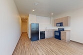 Located at 14455 East Ellsworth Avenue in Aurora, Colorado, this one-bedroom, one-bathroom unit offers a well-organized single-floor layout designed for functional, everyday living. Light wood-style vinyl flooring runs consistently throughout, lending a clean and cohesive aesthetic to every room.

The open-concept living, dining, and kitchen area forms the heart of the unit. The kitchen features light wood laminate cabinetry, light stone-toned countertops, and a full suite of black appliances — including a refrigerator, electric range, dishwasher, and over-the-range microwave. Recessed lighting illuminates the space from above.

A hallway connects the main living area to the private spaces, and includes a built-in bench and wall-mounted coat hooks — a practical entryway nook ideal for everyday organization. The hallway leads to the bedroom, which is bright and airy thanks to two large windows dressed with vertical blinds, allowing abundant natural light. A wall-mounted HVAC unit provides individualized climate control.

The combined bathroom and laundry room is cleanly finished with a full soaking tub and shower, chrome hardware, and built-in shelving. The crisp white surround and wood-tone flooring keep the space feeling fresh and tidy. Overall, the unit presents a modern, no-frills design well-suited for practical, comfortable living.