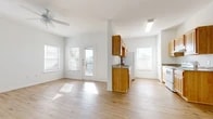 This single-floor residence offers a clean, functional layout designed to maximize natural light and ease of movement throughout. Light hardwood flooring runs continuously across all rooms, lending a warm, cohesive feel to the entire space.

The entry foyer welcomes visitors with a sidelit front door and direct access to the main living areas. The spacious living room is anchored by a ceiling fan, multiple windows, and a glass-panel door that opens to an outdoor area, filling the room with abundant natural light.

The kitchen is well-appointed with warm-toned wood cabinetry, granite-patterned countertops, and white appliances including a range, dishwasher, and refrigerator. A dedicated window above the sink area brightens the workspace, while ample upper and lower cabinetry provides generous storage.

A peninsula-style counter divides the kitchen from an adjacent dining or flex space, also outfitted with a ceiling fan and rear door access. The bedrooms are generously proportioned, each featuring light-filled windows with blinds and clean white walls that offer a versatile blank canvas. The bathroom includes a full soaking tub with surround, a toilet, wood cabinetry, and granite countertop detailing consistent with the kitchen. The overall ambiance is bright, airy, and move-in ready.