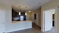 This single-floor residence features an open-concept layout that seamlessly connects the kitchen and living areas, creating a spacious and functional environment. The kitchen is appointed with dark espresso cabinetry that contrasts elegantly with light countertops, offering ample storage and workspace. A peninsula with an integrated sink serves as a natural divider between the kitchen and the adjoining living space, ideal for casual dining or entertaining. Stainless steel appliances, including a full-size refrigerator and range, add a contemporary touch, while a built-in microwave above the stove maximizes efficiency.

Pendant lighting hangs above the peninsula, providing both task illumination and a decorative focal point. The flooring throughout is a warm hardwood-style surface that adds continuity and a clean aesthetic. Neutral-toned walls complement the overall palette, lending the space a bright and welcoming ambiance. Near the entryway, white panel doors open to a closet or storage area, offering practical organization options. A secondary doorway leads further into the unit, suggesting additional private rooms beyond the main living area.