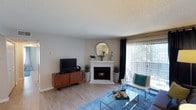 This single-floor residence offers a thoughtfully designed layout with a cohesive modern aesthetic throughout. The living room serves as the central gathering space, highlighted by a white brick fireplace with a decorative mantle, light wood-style flooring, and a large sliding glass door fitted with vertical blinds that admits generous natural light and provides access to an outdoor area with views of surrounding greenery. The space accommodates a comfortable seating arrangement and glass-top coffee table, anchored by a vibrant area rug.

The kitchen features a galley-style layout with white upper cabinetry, dark lower cabinets, stainless steel appliances including a refrigerator, microwave, and range, and a blue tile backsplash. A peninsula with a white countertop and integrated sink opens toward the living area, enhancing the functional flow of the space.

Multiple bedrooms offer wood-style or carpeted flooring, neutral wall tones, textured ceilings, and windows with blinds or sheer curtains providing natural light. Each room includes closet access and sufficient space for a full or queen-sized bed with additional furnishings.

The bathroom includes a full tub-shower combination with white tile surround, hexagonal accent tile, and clean white fixtures throughout.
