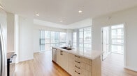 Located at 1150 E Street in the heart of downtown San Diego, this modern 2-bedroom, 2-bathroom residence offers a thoughtfully designed open-concept floor plan with high-end finishes throughout. Light hardwood flooring flows seamlessly through the living, dining, and kitchen areas, complemented by recessed lighting and crisp white walls that enhance the bright, airy atmosphere.

The kitchen serves as a central hub of the space, featuring a large island with a quartz countertop and double undermount sink, light wood cabinetry, a full suite of stainless steel appliances including a French door refrigerator, microwave, and electric range, and a classic subway tile backsplash. The open layout connects effortlessly to the dining and living areas.

Floor-to-ceiling windows frame sweeping panoramic views of the San Diego skyline, flooding the living spaces with natural light. A private balcony accessible from the living area extends the living space outdoors.

Both bedrooms continue the hardwood flooring and benefit from expansive window walls with city views. Each bedroom is served by ample closet space. The two bathrooms are finished with marble-style tile flooring and wall surrounds, wood-toned vanities, and soaking tub and shower combinations. A hallway connects all areas efficiently, completing this well-appointed urban residence.