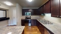 This single-floor residence located at 3944 Edinbrook Terr N in Brooklyn Park, Minnesota offers a well-designed layout with functional living spaces throughout. The open-concept kitchen is a standout feature, showcasing rich dark espresso cabinetry, granite-style countertops, hardwood-style flooring, and a central island with a rounded edge — ideal for casual dining or meal prep. Stainless steel appliances, including a range, microwave, and dishwasher, are complemented by a black refrigerator, completing a practical and stylish culinary space. The kitchen flows seamlessly into the living area, which is generously sized and finished with plush neutral carpeting. Large windows fitted with horizontal blinds allow ample natural light to fill the room, offering views of the surrounding greenery. An exterior door in the living area provides convenient outdoor access. The bedroom is a comfortable, carpeted retreat with a wide window that frames outdoor views and allows natural light to brighten the space. The full bathroom features a tub-shower combination with white tile surround, a toilet, and a vanity topped with granite-style countertops and a white basin sink, accented by brushed nickel fixtures and a large wall mirror. Textured ceilings are consistent throughout the residence, adding a classic finishing detail to every room.