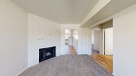 This single-floor unit offers a thoughtfully laid-out living space with a clean, neutral palette throughout. The living room serves as the heart of the home, anchored by a striking floor-to-ceiling white brick fireplace wall that adds character and texture to the space. Soft carpet flooring extends across the living area and bedrooms, providing warmth underfoot.

The kitchen is well-equipped and functional, featuring white cabinetry, dark granite-style countertops, a peninsula for additional workspace, and a full suite of white appliances including a refrigerator, electric range, and dishwasher. A large window above the sink allows natural light to fill the space, and durable wood-look flooring ties the kitchen together.

The bedrooms are comfortably sized, each outfitted with carpet flooring and built-in closets. The primary bedroom includes a sliding glass door that opens to an outdoor area, bringing in additional natural light and providing a pleasant connection to the exterior.

The bathroom is clean and straightforward, offering a full tub-shower combination, a toilet, and a vanity with dark countertop and under-sink cabinetry, all finished with wood-look flooring. The overall design is simple and functional, presenting a move-in-ready space with a bright, open atmosphere.