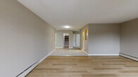 Located at 14965 107A Ave in Surrey, BC, this single-floor, 3-bedroom, 1-bathroom unit offers a practical and comfortable layout finished in a neutral, modern palette. The open living and dining area is a standout feature, bathed in natural light through large windows and a sliding glass door that leads directly to a private patio with outdoor views of mature trees and greenery. Light-toned hardwood flooring flows throughout the main living spaces, complementing the warm beige tones on the walls and crisp white baseboards. The kitchen is efficiently designed with white cabinetry, a marble-patterned countertop, a subway tile backsplash, tile flooring, and a full-size refrigerator. A central hallway connects the three bedrooms, each featuring light hardwood floors, baseboard heating, and windows overlooking the surrounding greenery, filling the rooms with natural light. Ample storage is provided by seven closets distributed throughout the unit. The bathroom is finished with tile flooring, a vanity with a dark granite-style countertop, white cabinetry, and a tiled shower surround. The overall ambiance is clean, bright, and move-in ready, suited to a variety of living arrangements.