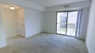 This single-floor residential unit offers a practical and comfortable layout designed for everyday living. The kitchen is well-appointed with an abundance of warm wood-toned cabinetry that provides generous storage space. It features a gas range, a dishwasher, a full-size refrigerator, and a double-basin sink with a modern faucet. Light-colored countertops complement the cabinetry, and tile flooring throughout the kitchen adds durability and ease of maintenance. The overhead ventilation hood and flush-mount ceiling light ensure the kitchen remains well-lit and functional. The living area is bright and open, featuring wall-to-wall carpeting that adds warmth underfoot. Large sliding glass doors flood the space with natural light and provide direct access to a private outdoor deck, offering pleasant views of the surrounding greenery and neighboring structures. The clean, neutral-toned walls throughout the living area create a versatile backdrop suitable for a variety of furnishing styles. A ceiling vent ensures consistent climate control throughout the space. Together, the rooms present a cohesive, low-maintenance living environment that balances practicality with comfort.