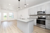 Located in Idaho Falls, ID, this well-designed one-bedroom, one-bathroom unit offers a thoughtful layout across a single floor. The kitchen serves as a standout centerpiece, featuring a large quartz-topped island with an undermount sink, white shaker-style cabinetry extending to the ceiling, and a full suite of stainless steel appliances including a refrigerator, electric range, and built-in microwave. Stylish geometric pendant lights hang above the island, adding a modern touch. Light wood-look flooring flows throughout the main living areas, complementing the bright, neutral color palette. The living room is airy and open, benefiting from recessed lighting and a glass-panel door that leads to an outdoor balcony, allowing natural light to pour in and offering pleasant views of the surrounding greenery. The bedroom is a comfortable retreat with plush carpeting, a large window with outdoor views, and ample wall space. The bathroom is finished with the same attention to detail, featuring white shaker vanity cabinets, a quartz countertop, a full tub-shower combo with tile surround, and wood-look flooring. A dedicated laundry room with full-size washer and dryer completes this efficient and modern living space.