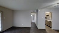 Located in Desoto, this single-floor home offers a clean and functional layout designed for comfortable everyday living. The main living area features dark hardwood-style flooring that extends throughout the space, providing a bold contrast against the bright white walls and textured ceiling. A central hallway leads from the living area toward the rear of the home, offering a clear sense of depth and connectivity between the various spaces. HVAC vents are integrated into the ceiling, ensuring efficient climate control throughout. To one side, a glimpse of the kitchen reveals cabinetry and tile work, suggesting a well-appointed cooking space. The overall interior presents a neutral color palette with white walls and a textured ceiling finish, creating a blank canvas that is both versatile and easy to personalize. The open sightlines between the living area, hallway, and kitchen contribute to an airy and cohesive feel throughout the home. With its straightforward single-level design and practical layout, this Desoto property is well-suited for a variety of lifestyles.