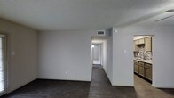 Located in Desoto, this single-floor home offers a clean and functional layout designed for comfortable everyday living. The main living area features dark hardwood-style flooring that extends throughout the space, providing a bold contrast against the bright white walls and textured ceiling. A central hallway leads from the living area toward the rear of the home, offering a clear sense of depth and connectivity between the various spaces. HVAC vents are integrated into the ceiling, ensuring efficient climate control throughout. To one side, a glimpse of the kitchen reveals cabinetry and tile work, suggesting a well-appointed cooking space. The overall interior presents a neutral color palette with white walls and a textured ceiling finish, creating a blank canvas that is both versatile and easy to personalize. The open sightlines between the living area, hallway, and kitchen contribute to an airy and cohesive feel throughout the home. With its straightforward single-level design and practical layout, this Desoto property is well-suited for a variety of lifestyles.