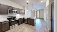Located at 3000 N Stemmons Fwy in Lewisville, Texas, this one-bedroom, one-bathroom residence offers a thoughtfully designed layout with modern finishes throughout. The open-concept kitchen serves as the centerpiece of the living area, showcasing rich dark cabinetry, gleaming granite countertops, a peninsula with an undermount sink, and a full suite of stainless steel appliances including a refrigerator, range, microwave, and dishwasher. Stylish globe pendant lights illuminate the kitchen, which flows seamlessly into the living area. Light wood-style flooring runs throughout the main living spaces, adding warmth and continuity. The living area is brightened by a large glass door that opens to a balcony, offering views of the surrounding community, and is equipped with a ceiling fan for added comfort. The bedroom features plush carpeting, a ceiling fan, and a window with blinds that allows natural light to filter in. The bathroom is finished with a granite-topped vanity with dark cabinetry, a glass-enclosed shower, wood-style flooring, and direct access to a dedicated walk-in closet with built-in shelving. The closet is carpeted and provides generous storage. Clean white walls and modern fixtures throughout give the space a bright, contemporary ambiance.