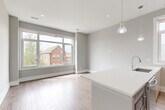 Located in Chicago's vibrant Pilsen neighborhood, this modern 3-bedroom, 2-bathroom home offers a thoughtfully designed single-floor layout. The open-concept living and kitchen area is bathed in natural light from large sliding windows that frame views of the surrounding neighborhood. Light hardwood floors flow throughout, complementing the neutral gray walls and crisp white trim. The contemporary kitchen features sleek, high-gloss cabinetry, a large white quartz waterfall island with an undermount sink, stainless steel appliances including a French door refrigerator, a statement range hood, and pendant lighting that adds warmth to the space. The bathrooms are finished with modern floating vanities, expansive mirrors, chrome fixtures, and tiled walk-in showers. The bedrooms are well-proportioned, with the primary bedroom offering closet access and proximity to a full bath. One bedroom opens directly onto a private balcony equipped with black metal railings, where sweeping views of the Chicago skyline — including Willis Tower — serve as a remarkable backdrop. A hallway connects the living areas to the bedrooms, maintaining a clean and functional flow throughout this stylish urban home.