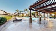 Located at 26660 E Ninth St in Highland, California, this beautifully designed outdoor amenity area offers a resort-inspired retreat for residents. The centerpiece is a generously sized swimming pool with crystal-clear blue water, complemented by a separate spa for relaxation. The expansive concrete pool deck is thoughtfully appointed with cushioned chaise lounge chairs and patio umbrellas, providing ample space for sunbathing and leisure.

A striking pergola structure, featuring rich dark wood beams supported by stone-clad columns, anchors one end of the deck and provides a shaded gathering area. Tall, mature palm trees are strategically placed throughout the space, enhancing the tropical, resort-like ambiance. Lush landscaping and manicured greenery frame the perimeter, adding privacy and visual appeal.

The surrounding residential buildings, finished in warm earth tones with balconies and pitched rooflines, create a cohesive and welcoming community atmosphere. The space benefits from an open, sun-drenched Southern California setting, and select vantage points reveal sweeping views of the nearby San Bernardino Mountains. A BBQ and outdoor dining area is also available, making this pool area an ideal setting for both relaxation and social gatherings year-round.