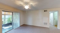 This single-story residence offers a practical and comfortable layout across several distinct areas. The living room serves as the central gathering space, finished with plush carpet and topped with a textured ceiling and a ceiling fan with integrated lighting. A sliding glass door fitted with vertical blinds opens to an outdoor patio, allowing natural light and greenery views to filter into the space. A secondary entry door with sidelights provides additional access.

The kitchen is well-appointed with warm wood-toned cabinetry offering generous storage, light-colored countertops, a peninsula with a breakfast bar, and wood-style flooring. White appliances include a refrigerator, electric range, and dishwasher, while a window above the sink brings in natural light. An adjacent dining area with pendant lighting completes the space.

The bedroom features carpet, a ceiling fan, a window with outdoor views, a walk-in closet, and direct access to a bathroom. The bathroom includes a tub and shower combination with white tile surround and chrome fixtures. An in-unit laundry area with washer and dryer hookups adds everyday convenience throughout this well-organized floor plan.