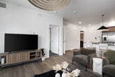 This thoughtfully designed one-bedroom, one-bathroom residence offers an efficient and stylish single-floor layout. The open-concept kitchen is a standout feature, boasting a large island with a dark stone countertop and bar seating, warm wood cabinetry paired with gray upper cabinets, a herringbone tile backsplash, and a full suite of stainless steel appliances. A bold pendant light anchors the space, creating a seamless transition into the living and dining areas. The living room is bright and airy, with light hardwood-style flooring and French doors that open to a private balcony, flooding the space with natural light and offering outdoor views. The bedroom provides a comfortable retreat, featuring plush carpeting, a large window with outdoor views, and clean white walls that create a calm, neutral atmosphere. The bathroom is well-appointed with dual undermount sinks set in a white countertop, gray cabinetry with black hardware, a walk-in glass shower, and warm wood-look flooring. Throughout the residence, a consistent modern aesthetic is maintained with clean lines, neutral tones, and quality finishes, making this a highly functional and visually cohesive living space.