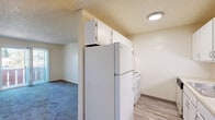 Located at 3801 Village Rd S in Colorado Springs, CO, this one-bedroom, one-bathroom unit offers a practical and well-organized single-floor layout. The living area features plush carpeting and neutral walls beneath a textured ceiling, creating a clean, comfortable atmosphere. A sliding glass door opens directly onto a private balcony with a classic red wood railing, offering views of mature pine trees and the surrounding Colorado Springs streetscape under open blue skies.

The galley-style kitchen is efficiently designed, with white cabinetry lining both sides, light wood-look vinyl flooring, a stainless steel sink, and white appliances including a refrigerator and range. Upper and lower cabinets provide ample storage throughout.

The bedroom is a well-proportioned, carpeted room with a large window dressed with vertical blinds that allows natural light to filter in. It includes access to a dedicated closet, providing convenient storage. A connecting hallway links the main spaces with a sense of flow and privacy.

The bathroom is clean and straightforward, featuring a full tiled tub and shower combination with white square tiles and chrome fixtures. The overall ambiance of the unit is functional and move-in ready, suited for comfortable everyday living in a convenient Colorado Springs location.