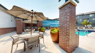 Located at 10320 Commonwealth St in Lone Tree, Colorado, this thoughtfully designed outdoor amenity space offers a resort-style experience centered around a large, crystal-clear swimming pool with an adjacent spa. The pool deck is generously sized, providing ample room for lounging on plentiful sling-style chaise chairs arranged along the pool's edge and throughout the surrounding sundeck areas. Mature shade trees are strategically placed throughout the space, offering natural relief from the Colorado sun while adding a lush, inviting atmosphere enclosed by a decorative wrought-iron perimeter fence.

A striking painted mural serves as a focal backdrop along one pool-facing wall, adding a vibrant artistic element to the outdoor environment. A pergola structure with clean, modern lines anchors a shaded outdoor dining area furnished with umbrella tables and chairs, ideal for gathering and socializing. Brick columns throughout lend a classic, durable architectural character that is complemented by the contemporary gray siding of the surrounding buildings.

The covered outdoor kitchen area is a standout feature, equipped with multiple stainless steel grills, granite countertops, and brick surround construction, providing a fully functional space for outdoor cooking and entertaining. Together, these elements create a cohesive, amenity-rich outdoor environment designed for relaxation and community engagement.