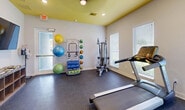 This 290 square foot fitness space in Florida City, FL, offers a well-equipped environment for exercise enthusiasts. The single-floor layout maximizes functionality within its compact footprint. The room features a variety of modern exercise equipment, including cardio machines like treadmills and ellipticals, as well as strength training apparatus.

The space boasts a bright and energetic atmosphere, enhanced by a vibrant yellow ceiling that contrasts nicely with the crisp white walls. Large windows with horizontal blinds allow natural light to flood the area, creating an airy feel and providing glimpses of the outdoor greenery.

The flooring consists of durable, dark-colored material suitable for workout activities. Wall-mounted storage solutions and cubbies offer convenient spaces for personal belongings and fitness accessories. Colorful exercise balls and other versatile equipment add to the room's dynamic ambiance.

A striking abstract painting in yellow, blue, and red tones adorns one wall, injecting a touch of artistic flair to the space. The combination of functionality and aesthetic appeal makes this compact fitness area an inviting spot for personal or small group training sessions.