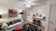 This single-story residence on E Valley Water Mill Road in Springfield, Missouri offers a well-organized layout designed for comfortable everyday living. The open-concept living area serves as the heart of the unit, featuring a textured ceiling, a ceiling fan with integrated lighting, and neutral carpet flooring. A bold black-and-white area rug anchors the space, which connects seamlessly to the kitchen via a raised breakfast bar with seating for two bar stools, making it ideal for casual dining or entertaining.

The galley-style kitchen is efficiently arranged with white cabinetry, gray laminate countertops, tile flooring, and a full suite of white appliances including a refrigerator, electric range, and over-the-range microwave. A secondary utility area with a double-basin sink and additional cabinetry provides extra workspace and storage.

The bedroom accommodates a full-sized bed comfortably, with carpet flooring, a ceiling fan, a window allowing natural light, and sufficient wall space for furnishings. The bathroom features a tub and shower combination enclosed by sliding glass doors, complementing the home's functional design.

Throughout, the unit maintains a cohesive, neutral color palette with consistent ceiling fans and ample built-in storage, creating a practical and organized living environment.