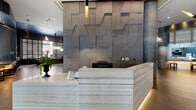 The lobby at 611 S Street in Baltimore, MD is a expansive, modern space that makes a striking first impression. Upon entry, residents and guests are greeted by a sculptural reception desk clad in layered marble, set against a dramatic three-dimensional textured metal accent wall that serves as the lobby's focal centerpiece. Soaring coffered ceilings with dark-painted exposed grid details add architectural depth, while large steel-framed windows flood the space with natural light and offer views of the surrounding streetscape.

The lounge area is anchored by a statement chandelier composed of cascading gold and silver rods, illuminating a curated seating arrangement of curved sofas, sculptural lounge chairs, and a linear gas fireplace set into a faceted stone feature wall. Polished concrete columns punctuate the open floor plan, seamlessly connecting distinct zones throughout the lobby.

A game area with a billiards table and contemporary pendant lighting transitions into a social lounge equipped with a wet bar, wall-mounted television, and bar seating—ideal for resident gatherings. A dedicated leasing office, framed by sheer floor-to-ceiling curtains and pendant drum lights, provides a bright and professional environment. Warm hardwood and large-format tile flooring unify the entire space, reinforcing the lobby's cohesive, upscale urban aesthetic.