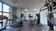 Located at 814 N 3rd St in Wilmington, NC, this single-floor fitness center is thoughtfully designed to support a well-rounded workout experience. The space features a drop-panel ceiling with recessed lighting that keeps the room bright and functional throughout. A rubberized flooring surface spans the entire area, providing both safety and comfort during exercise.

The cardio zone is anchored by multiple treadmills, including a Landice model, as well as an elliptical trainer and a stationary bike. Large floor-to-ceiling windows along one wall flood this section with natural light and offer views of the surrounding streetscape, creating an open and energizing atmosphere. A wall-mounted flat-screen television is positioned above the treadmill row for entertainment during workouts.

The strength training area features a multi-station cable machine that accommodates a wide variety of resistance exercises, complemented by a selection of benches, a power rack, and wall-mounted weight storage. A full-length mirror expands the visual depth of the space while assisting users with form and technique. A water cooler, sanitary dispensers, and a small waste receptacle ensure the space remains clean and convenient. Decorative abstract artwork on the walls adds a polished, contemporary aesthetic to the overall environment.