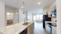 Located at 101 Pine Forest Rd in Augusta, Georgia, this single-floor residence offers a thoughtfully designed open-concept layout that seamlessly connects the kitchen, dining, and living areas. The kitchen serves as a focal point of the space, featuring a central island topped with granite countertops, a deep single-basin sink with a brushed gold faucet, and pendant lighting overhead. Light wood-tone cabinetry pairs elegantly with black appliances, including a refrigerator, range, microwave, and dishwasher. Wood-style plank flooring extends throughout the main living areas, adding warmth and continuity to the design. The living area is bright and airy, benefiting from natural light streaming through large windows and a sliding glass door that opens to an outdoor space. A ceiling fan keeps the area comfortable year-round. The bedroom features plush carpeting, a ceiling fan, and dual windows that invite additional natural light. The bathroom is well-appointed with granite-topped dual vanity, wood-tone cabinetry, a bathtub with shower, and matching wood-style flooring. A clean entryway hall provides a welcoming transition into the home. The overall aesthetic is modern and cohesive, with neutral tones and quality finishes throughout.