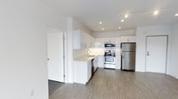 This single-floor space showcases a contemporary design with a clean, minimalist aesthetic. The kitchen is a standout feature, outfitted with a full suite of stainless steel appliances, including a refrigerator, electric range with double oven, built-in microwave, and dishwasher. Crisp white flat-panel cabinetry extends to the ceiling, maximizing storage capacity while contributing to the bright, open feel of the space. Light-toned countertops complement the cabinetry and provide ample workspace. A single-basin sink with a modern faucet is conveniently positioned beneath recessed cabinetry. The kitchen is thoughtfully separated from the adjacent area by a partial wall, creating a natural division while maintaining an open flow. Recessed lighting and track lighting illuminate the space effectively, enhancing the airy atmosphere. Light wood-style flooring runs throughout, adding warmth and continuity to the overall design. The neutral color palette of whites and soft grays creates a cohesive, modern environment that feels both functional and inviting.
