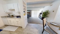 Located at 1111 Cardenas Dr SE in Albuquerque, New Mexico, this one-bedroom, one-bathroom unit offers a well-organized single-floor layout that maximizes functionality throughout. The open-concept living and dining area forms the heart of the space, where wood-look flooring in the dining zone transitions seamlessly into plush carpeting in the living room. Exposed ceiling beams add a subtle architectural detail, while a large sliding glass door floods the living room with natural light. A built-in shelving unit with cabinet storage elegantly divides the living area from the kitchen entry, adding both style and practicality. The kitchen features white cabinetry, granite-style countertops, and full appliances in a clean galley-style configuration. The dining area accommodates a full table and chairs beneath a ceiling fan, with two-tone wall treatment lending a polished touch. The carpeted bedroom is generously proportioned, offering access to a large walk-in closet with wire shelving and hanging rods, as well as a sliding glass door to an outdoor area. The bathroom includes a wide vanity with granite-style countertops, white cabinetry, and a shower-tub combination. Throughout, the unit maintains a bright, neutral palette that enhances the sense of openness.