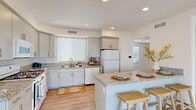 Located in Moreno Valley, CA, this contemporary three-story home offers 3 bedrooms, 4 bathrooms, and a well-organized layout across three distinct levels. The ground floor houses an attached garage with an automatic opener and clean concrete flooring, alongside an entrance that leads to the main living areas via wood-look staircases framed by bright white walls and natural light from slatted windows.

The main living level is the heart of the home, anchored by an open-concept kitchen outfitted with granite countertops, gray shaker cabinets, a gas range, and a peninsula with bar seating — ideal for casual dining. Recessed lighting and a statement ring pendant illuminate the space, while light-toned wood-look flooring runs seamlessly into the adjacent living room. A convenient full bathroom on this level adds practicality.

The upper floor hosts all three bedrooms, including a generously sized primary suite complete with a dedicated walk-in closet featuring wrap-around shelving. The bathrooms maintain a consistent, clean aesthetic with granite vanities and modern fixtures. A private balcony provides an outdoor retreat with open sky views.

Throughout, the home is finished with crisp white walls, wood-look flooring, and abundant natural light, creating a bright and cohesive atmosphere. The exterior features a fully fenced yard with white vinyl privacy fencing.